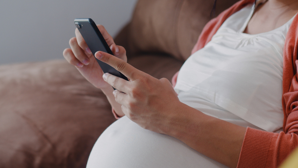 pregnant woman holding a cell phone, taking a pregnancy test using the app.